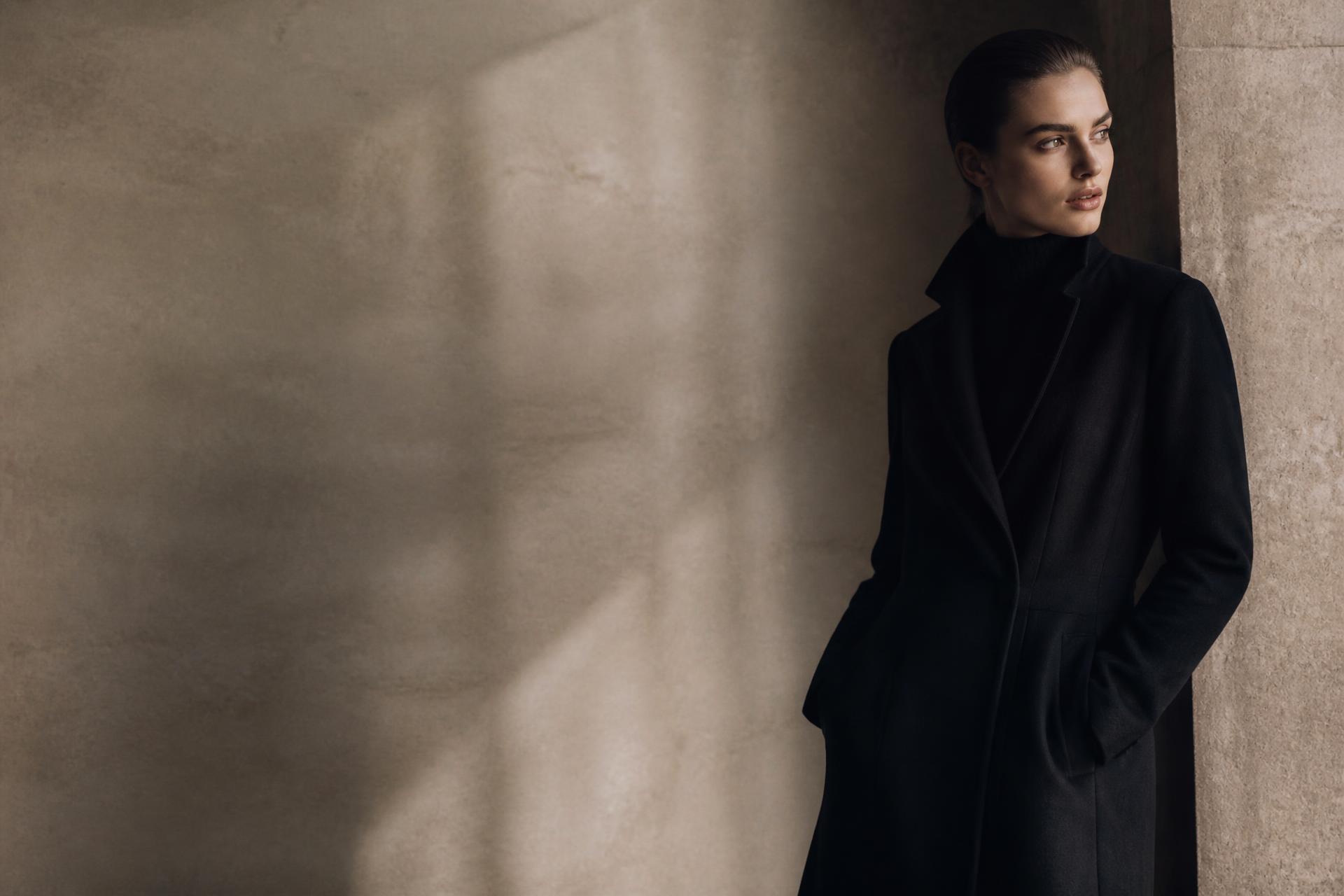 ODCORRECT editorial campaign — tailored black overcoat in a softly lit stone gallery